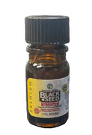 A small amber glass bottle of Black Seed supplement with a black ribbed cap and a yellow label, photographed on a dark surface with a blurred indoor background.