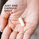 Hand holding a capsule with text 'JUST ONE CAPSULE DAILY' on a blurred background
